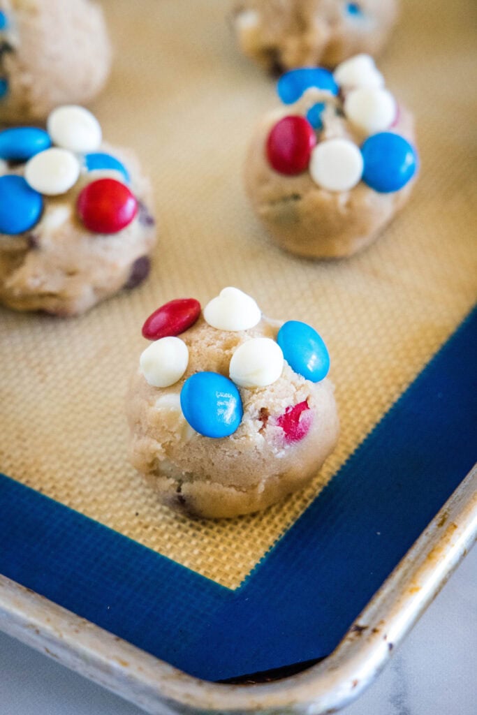 balls of cookie dough topped with white chocolate and M&M"s on a baking sheet