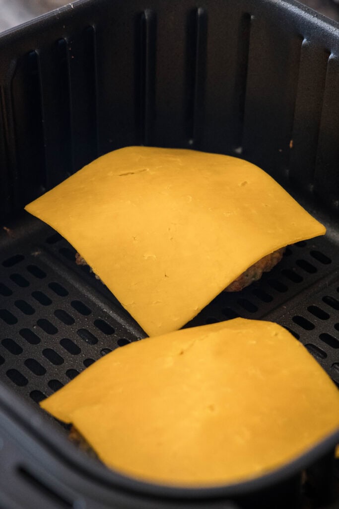 Slices of cheese laid over chicken patties in the air fryer.