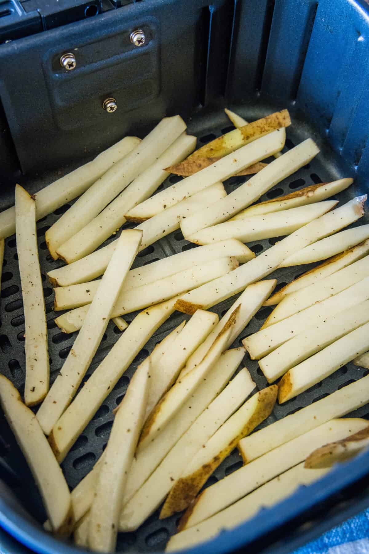 Uncooked homemade French fries inside the air fryer basket.