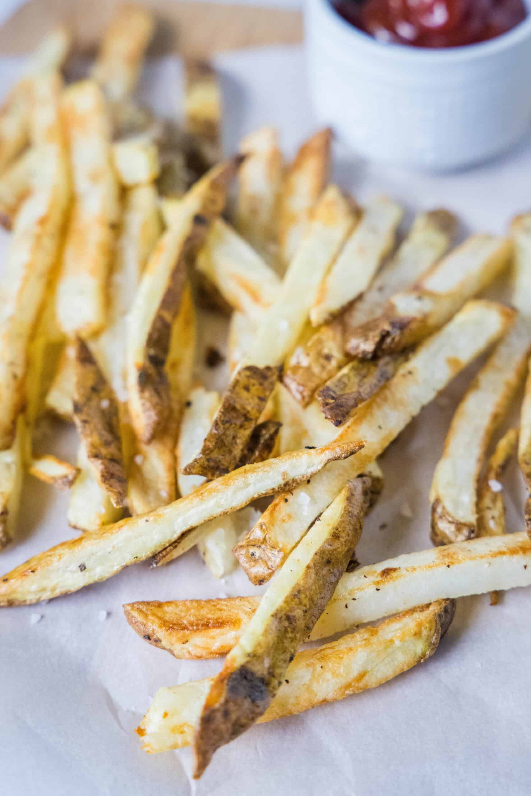 Homemade air fryer French fries on a sheet of parchment paper with a ramekin of ketchup in the background.