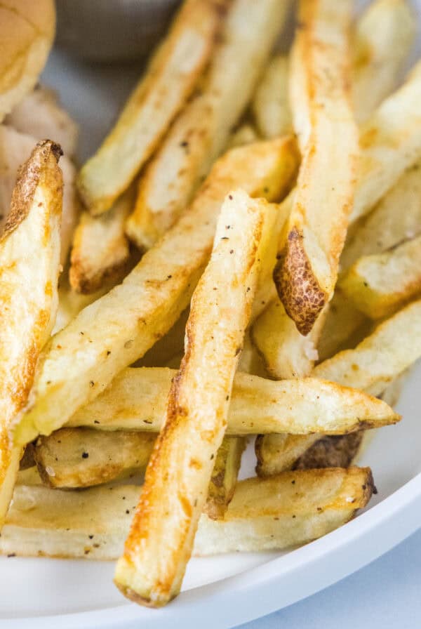 Close up of air fryer French fries next to a burger on a plate.