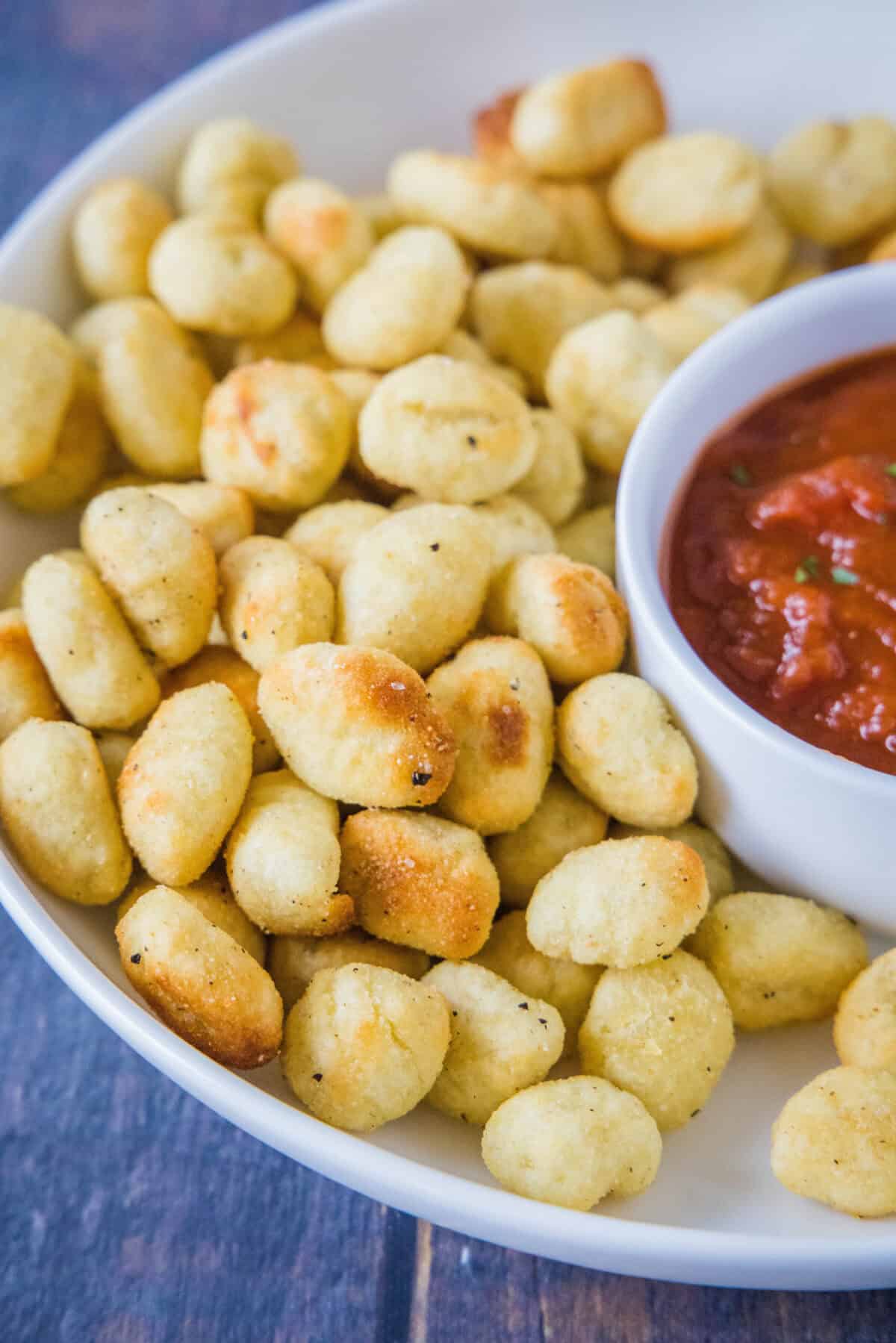 close up air fryer gnocchi on serving platter with bowl of marinara sauce