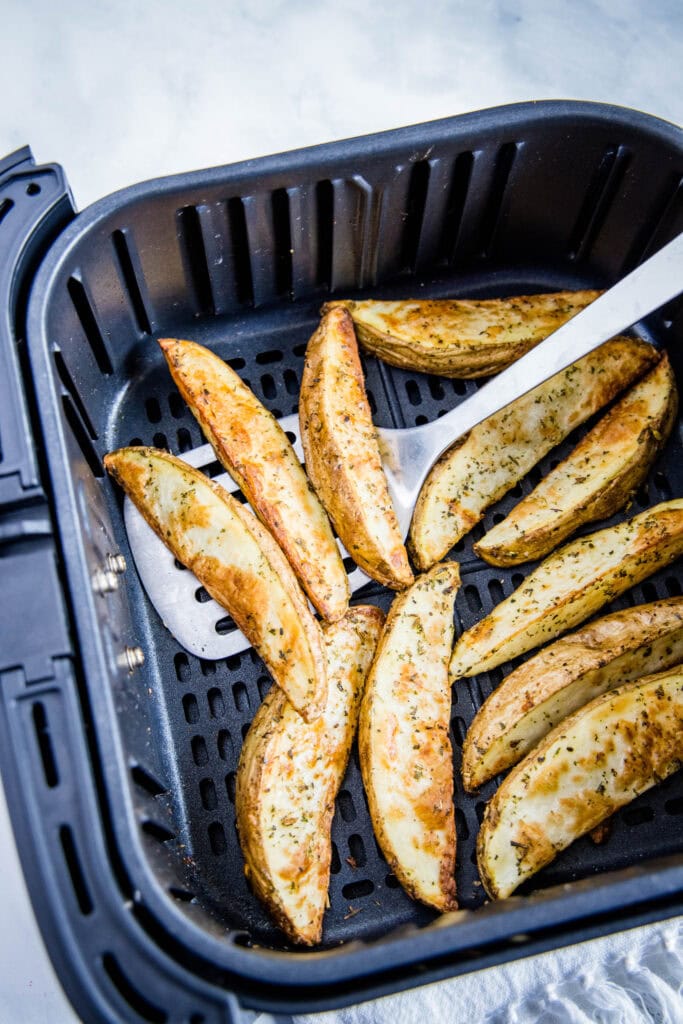 spatula removing cooked potato wedges from air fryer
