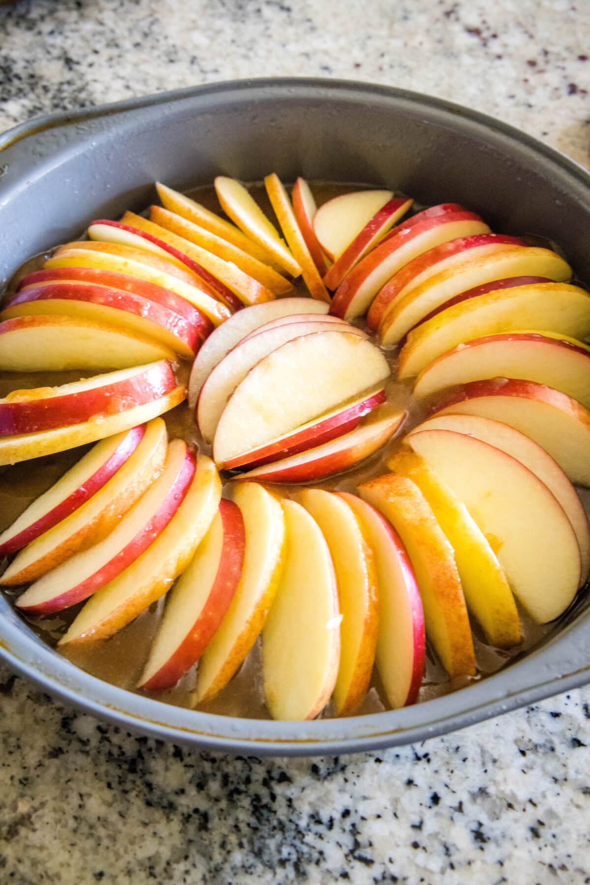Sliced apples arranged over top of the caramel layer in a round baking pan.