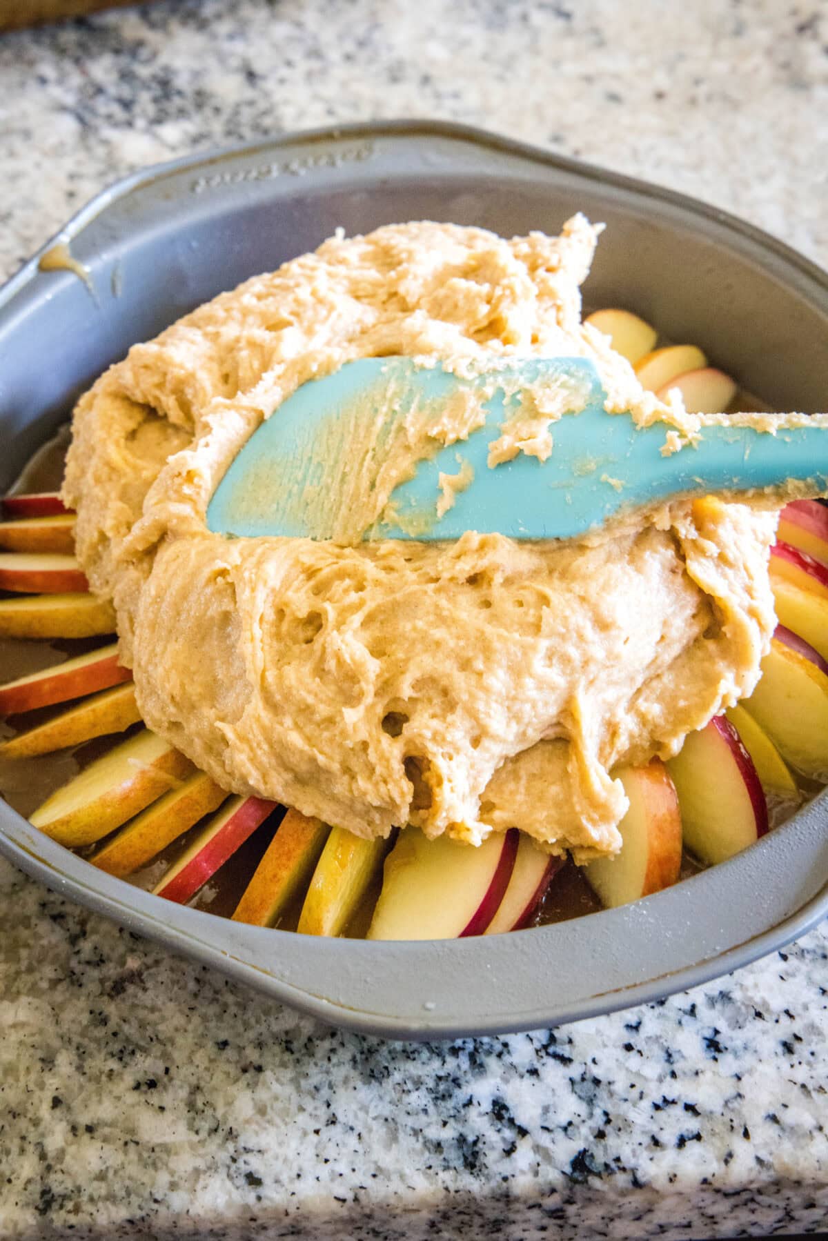 Cake batter being spread over top of the caramel apple layer in a round cake pan.