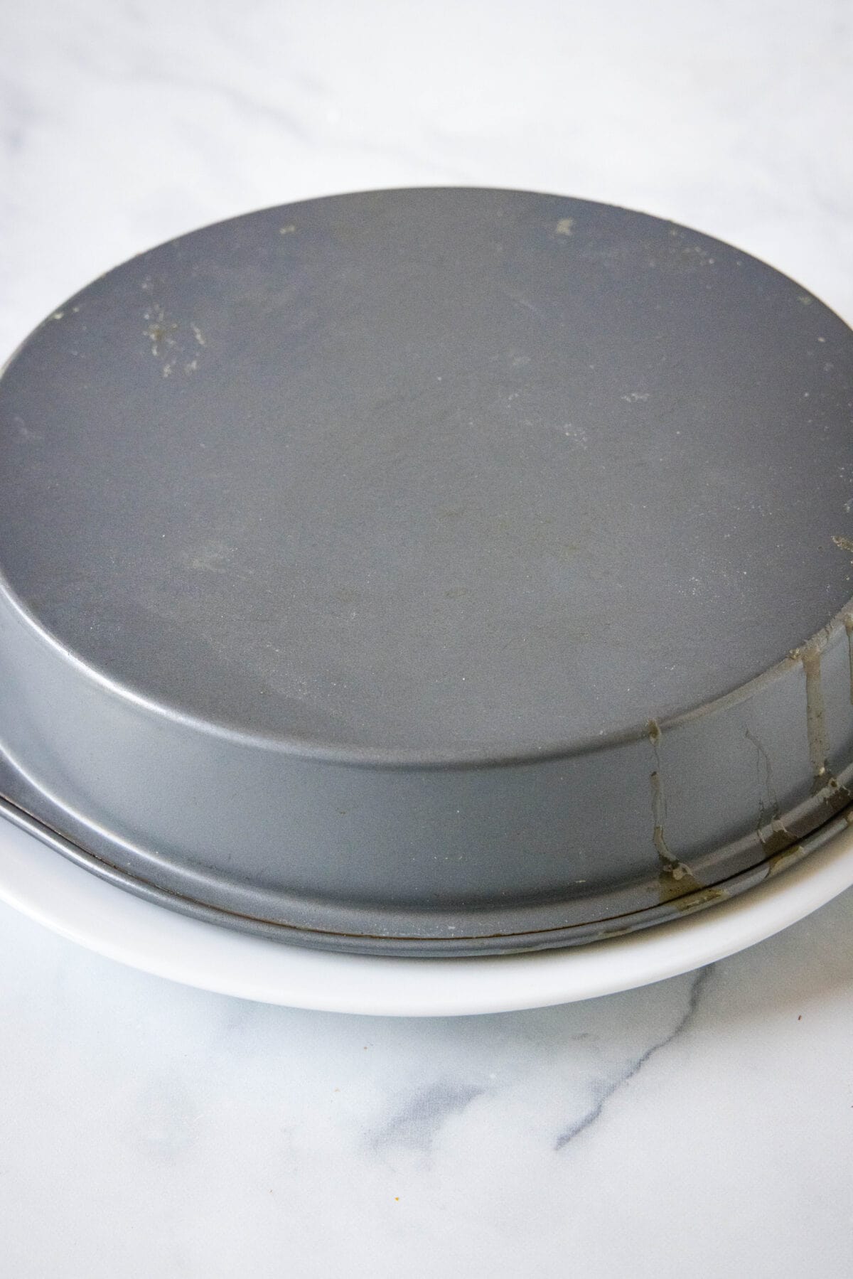 A round baking pan flipped upside down on a white plate, inverting the cake.