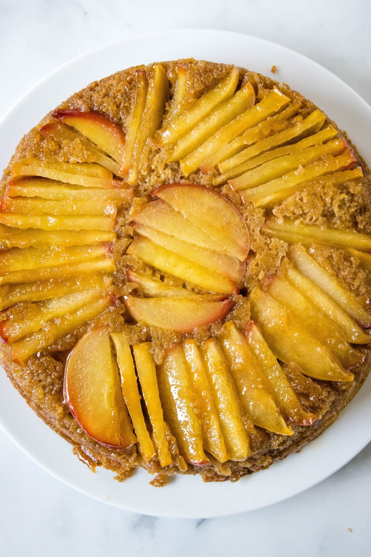 Overhead view of a whole apple upside down cake on a white plate.