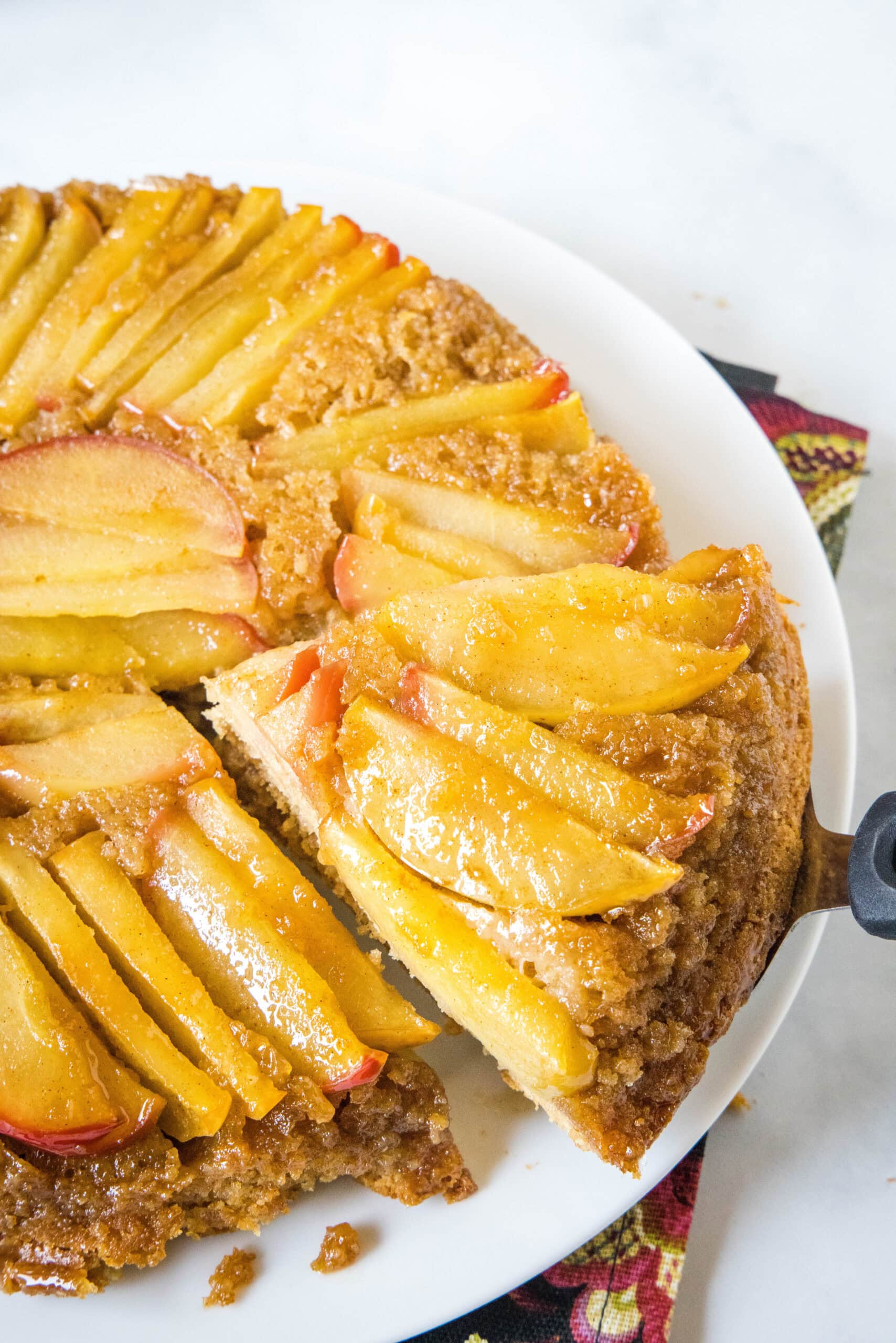 A slice of apple upside down cake being lifted from the rest of the cake on a white plate.