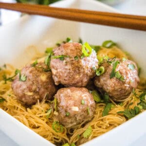 close up asian meatballs over rice noodles in a white bowl
