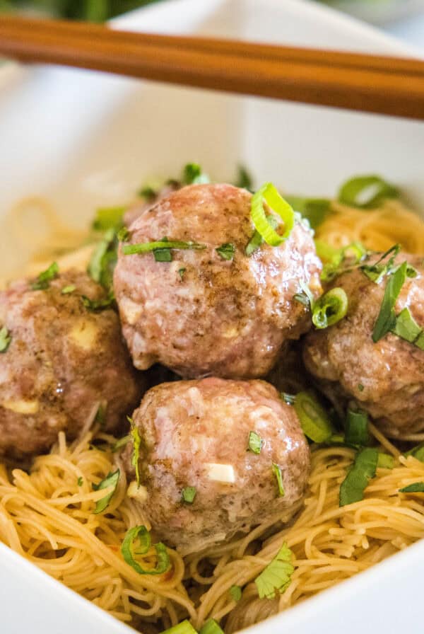 close up asian meatballs over rice noodles in a white bowl