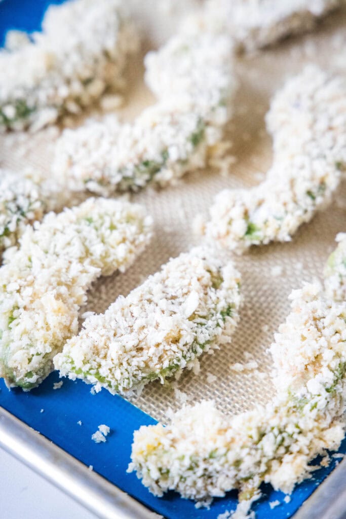 Breaded avocado slices arranged on a silpat lined baking sheet.