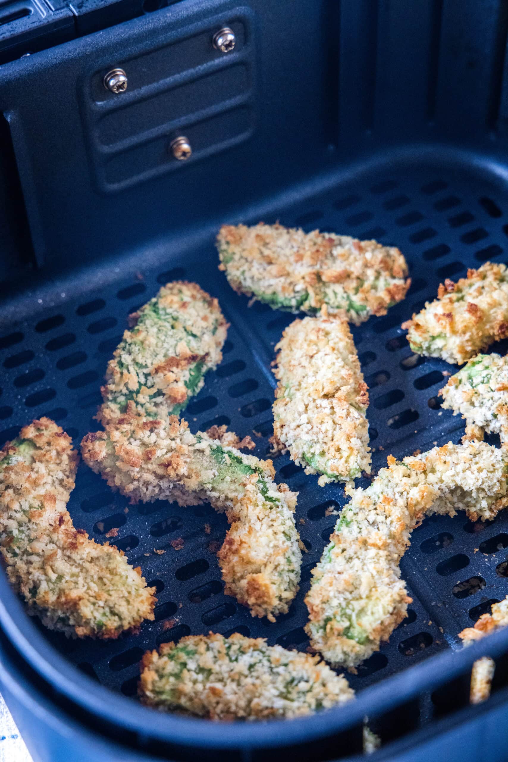 Avocado fries inside the air fryer basket.