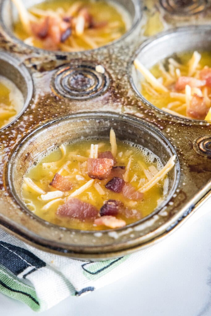 Muffin pan wells filled with unbaked bacon cheese egg muffin mixture.