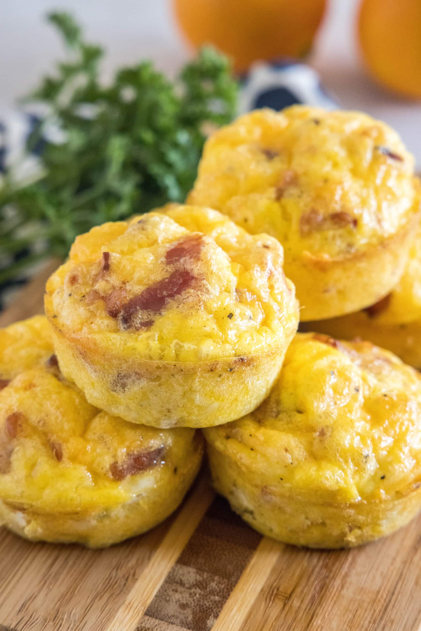 Bacon cheese egg muffins stacked on a wooden cutting board.