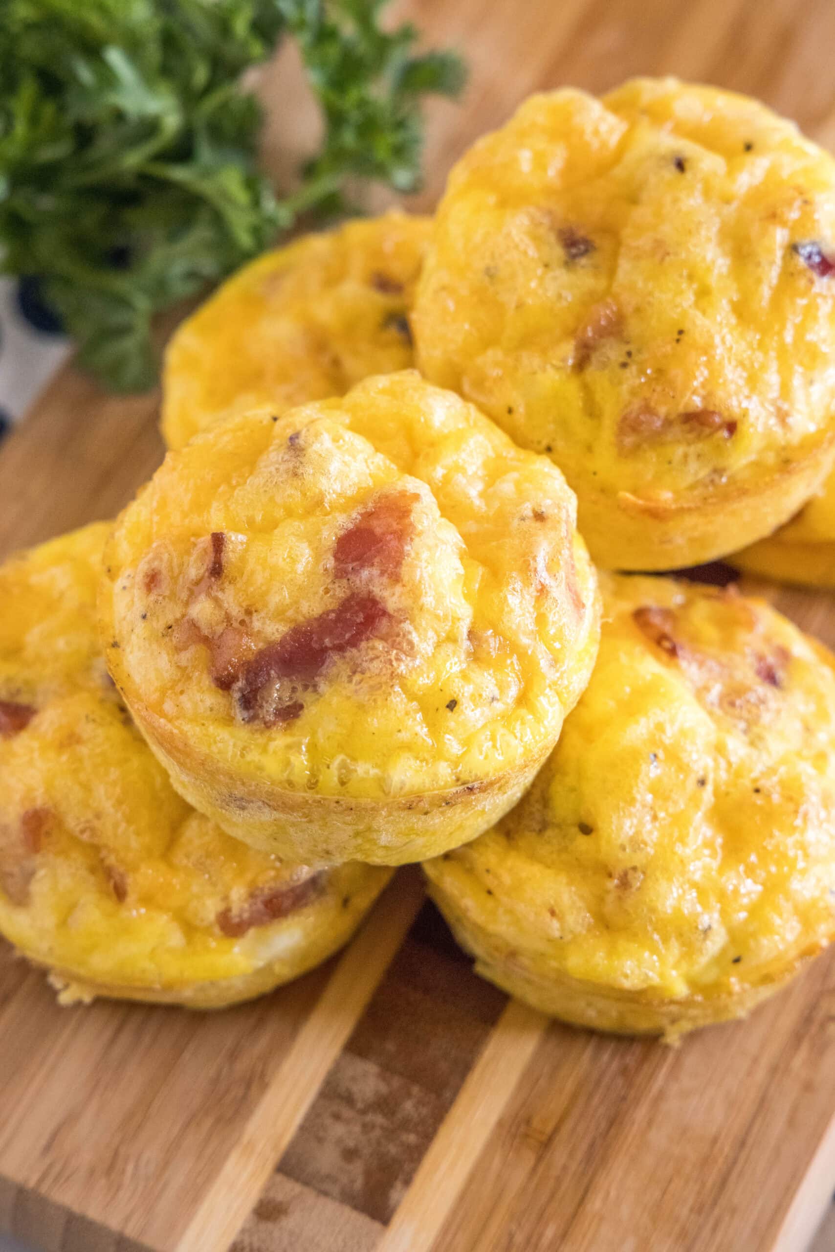 Bacon cheese egg muffins stacked on a wooden cutting board.