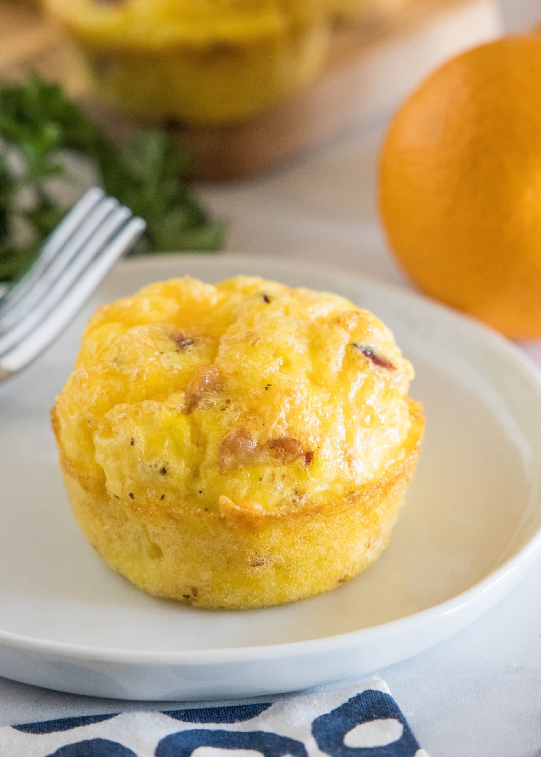 A bacon cheese egg muffin on a white plate next to a fork.