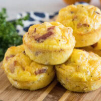 Bacon cheese egg muffins stacked on a wooden cutting board.