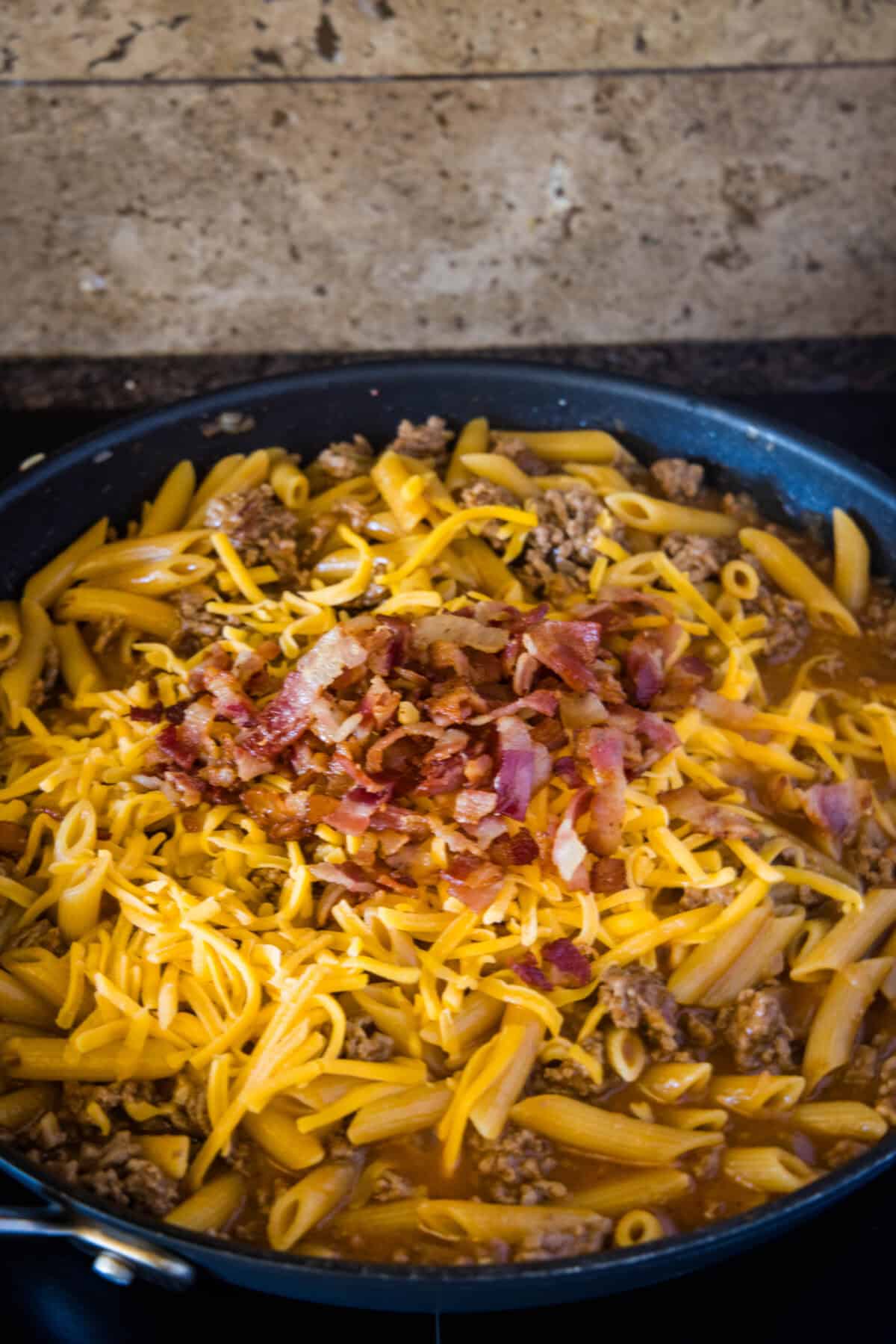 adding bacon and cheese to skillet of pasta