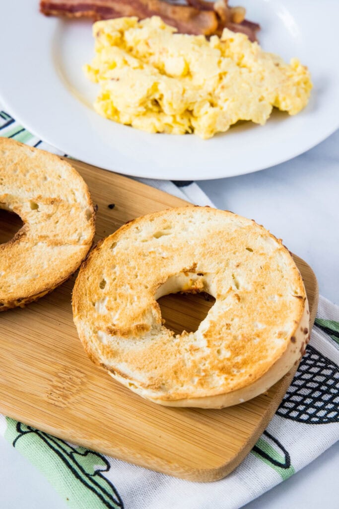 A toasted bagel next to a plate of eggs and bacon