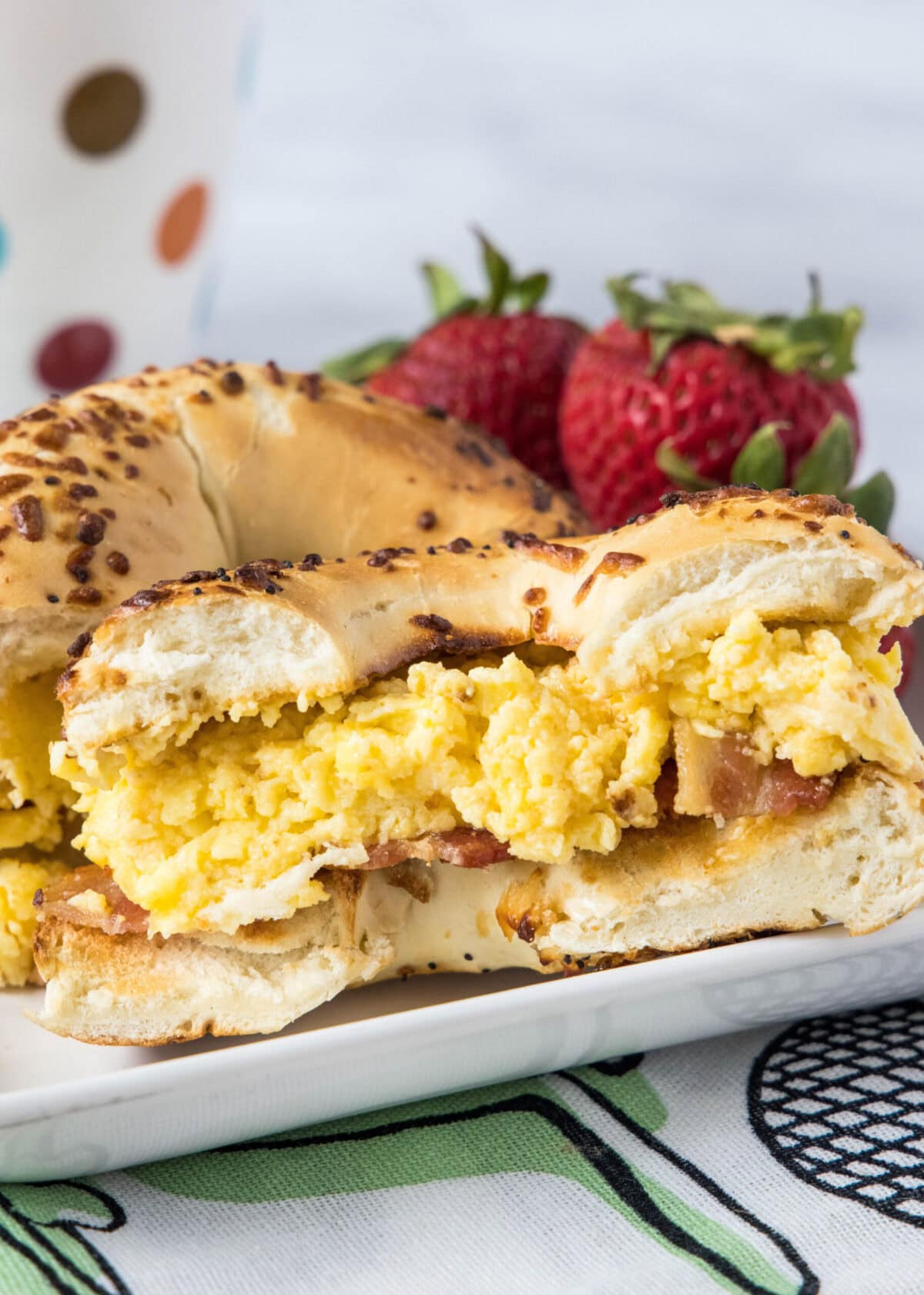 A bacon and egg breakfast sandwich cut in half on a plate with strawberries