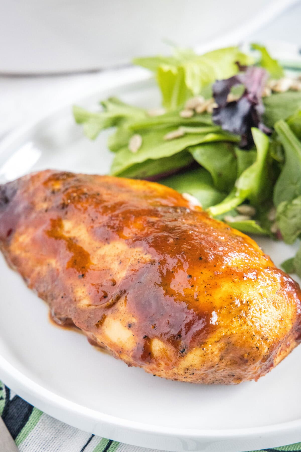 Oven baked BBQ chicken is juicy, tender, smoky, spicy, and has everything you love about barbecue, but without the smoke, hassle, or mess. A BBQ chicken breast on a plate with salad