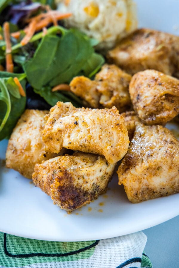 Baked chicken bites next to green salad on a plate.