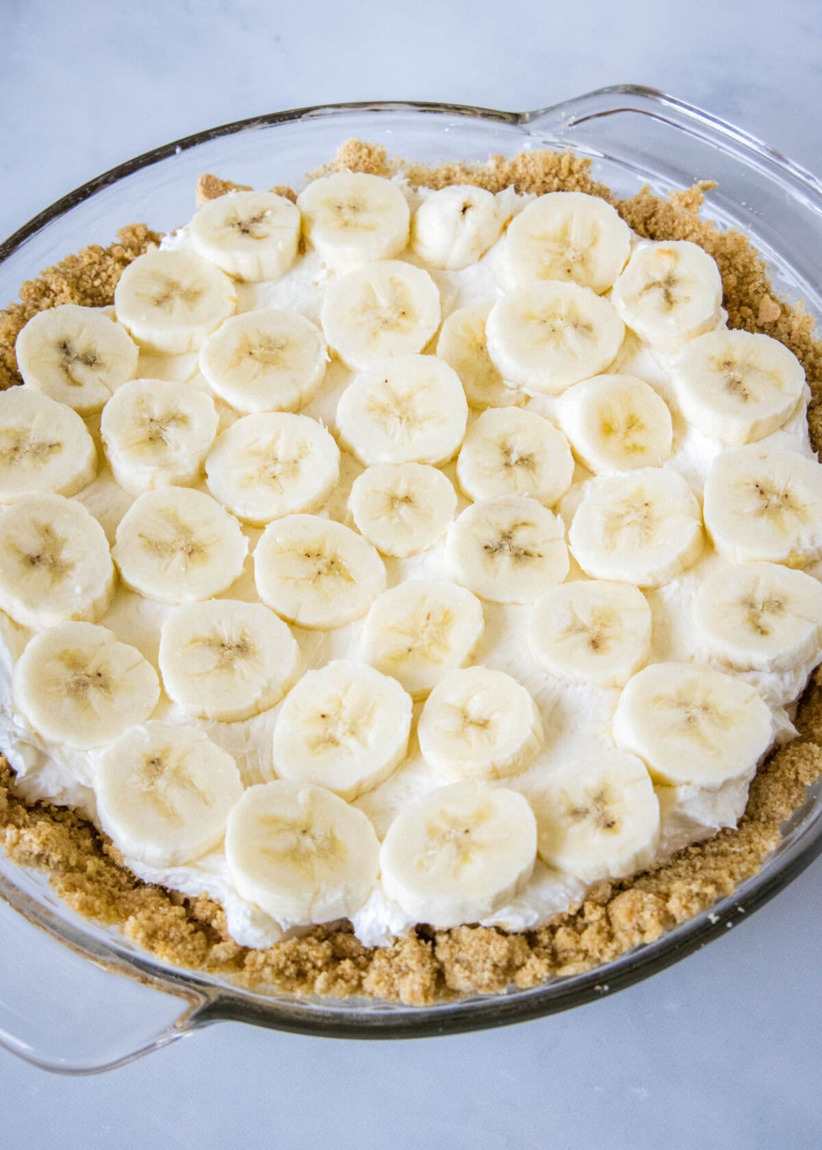 Banana slices layered over top cream cheese pie filling in a graham cracker crust.