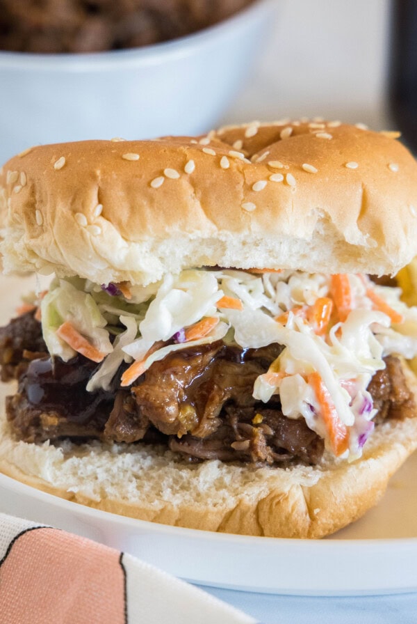 A BBQ beef sandwich with coleslaw on a white plate.