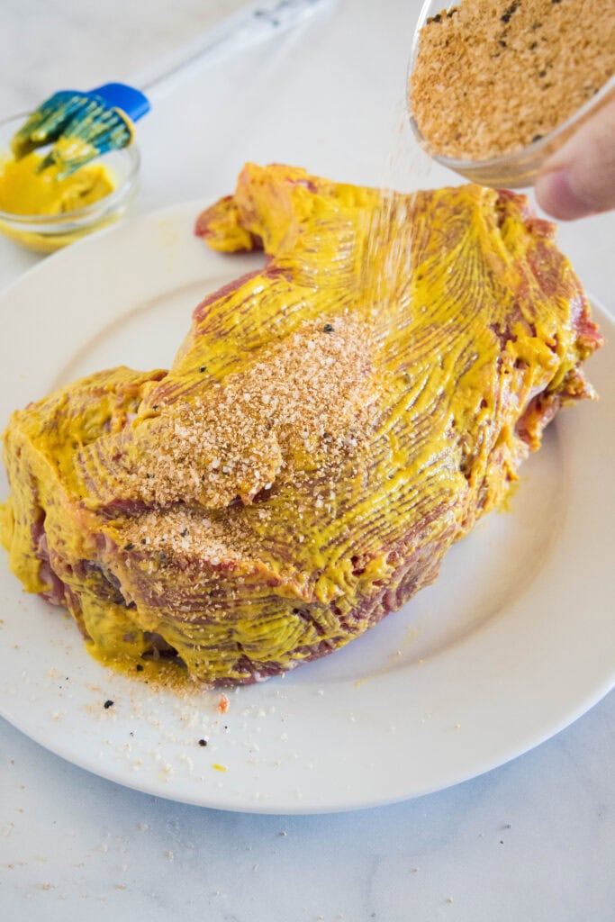 Chuck roast coated with mustard and dry rub on a white plate.