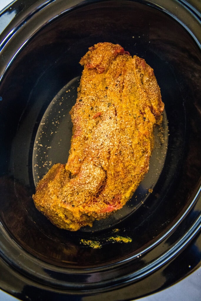 Chuck roast coated with mustard and dry rub inside the crock pot.