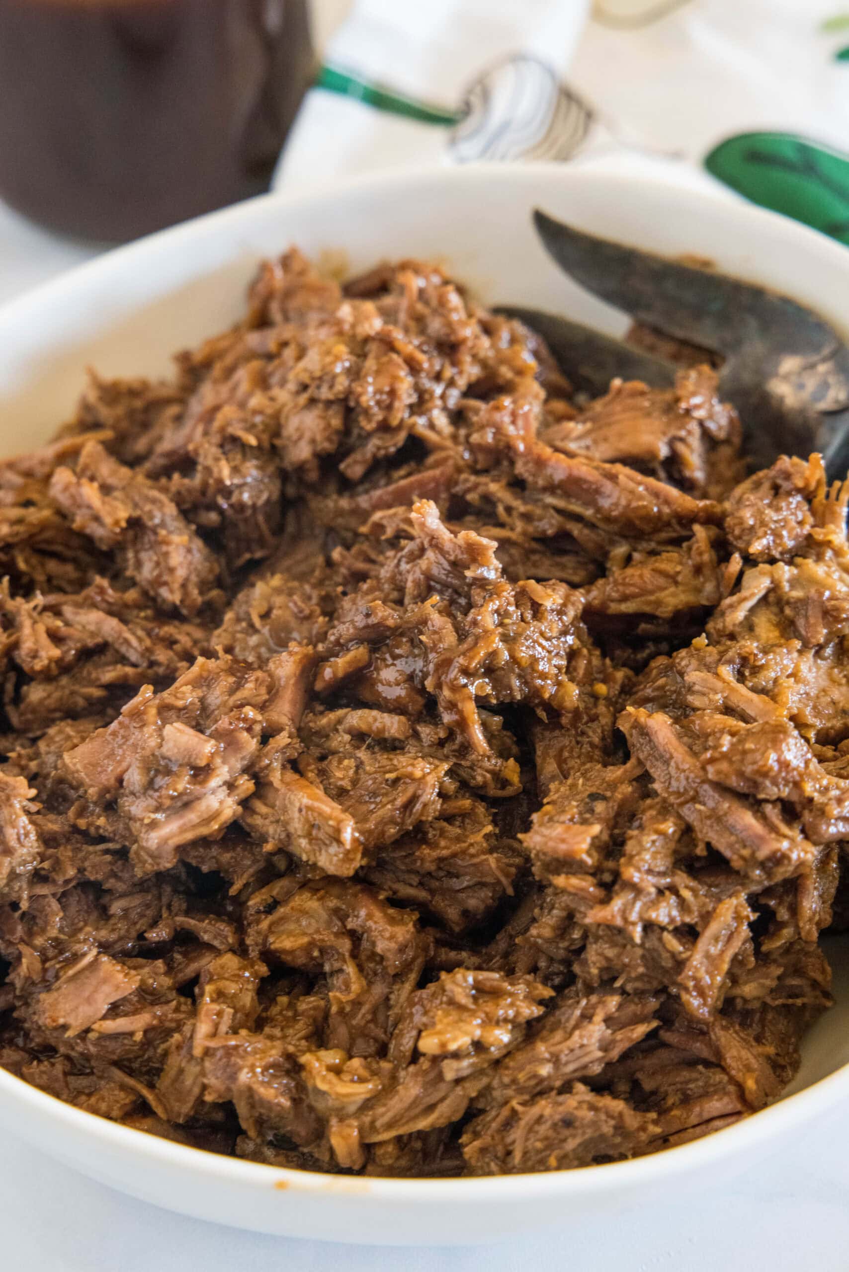 Metal tongs resting in shredded BBQ beef inside the crock pot.