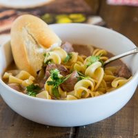A bowl of beef and noodle soup with bread