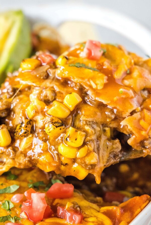close up scooping beef enchilada casserole out of the pan
