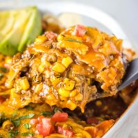 close up scooping beef enchilada casserole out of the pan