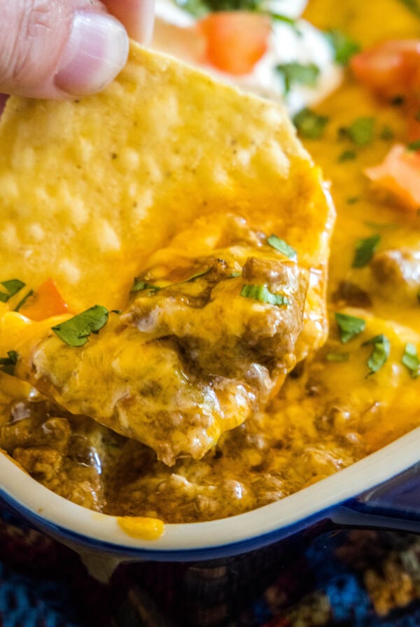 close up scooping enchilada dip out with a chip