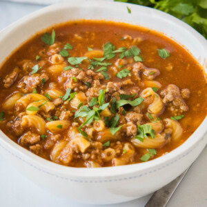 A bowl of beef macaroni soup garnished with fresh parsley.