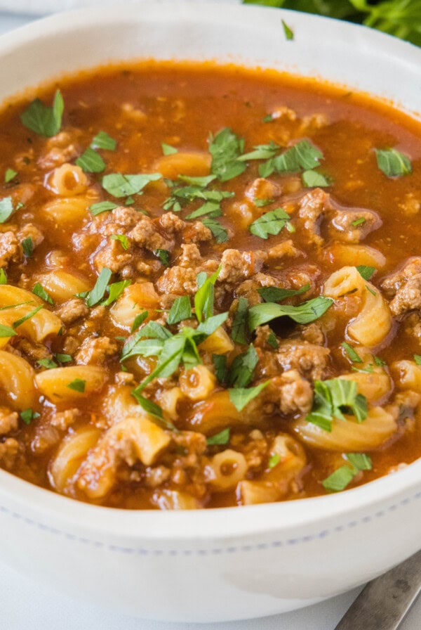 A bowl of beef macaroni soup garnished with fresh parsley.