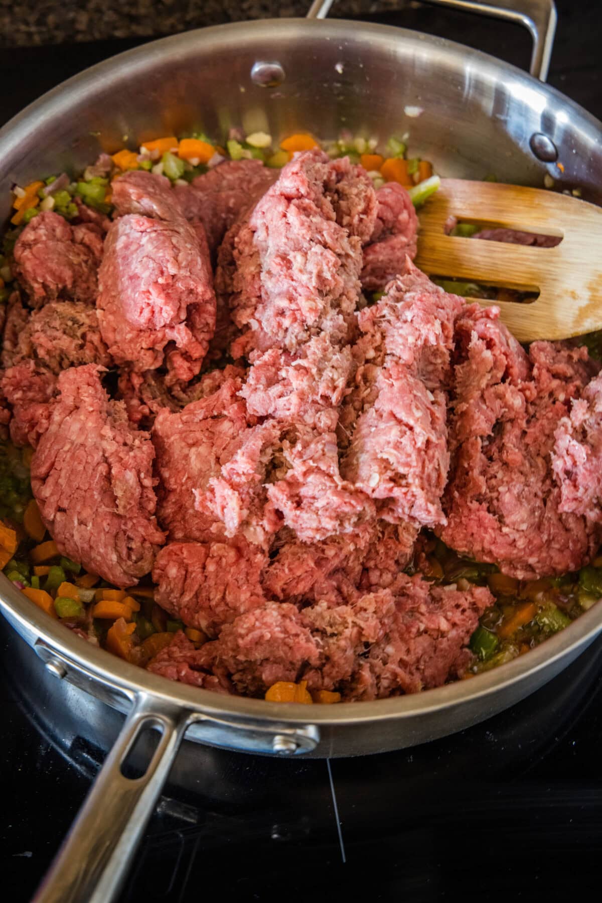 Ground beef partially broken up in a skillet with a wooden spatula.