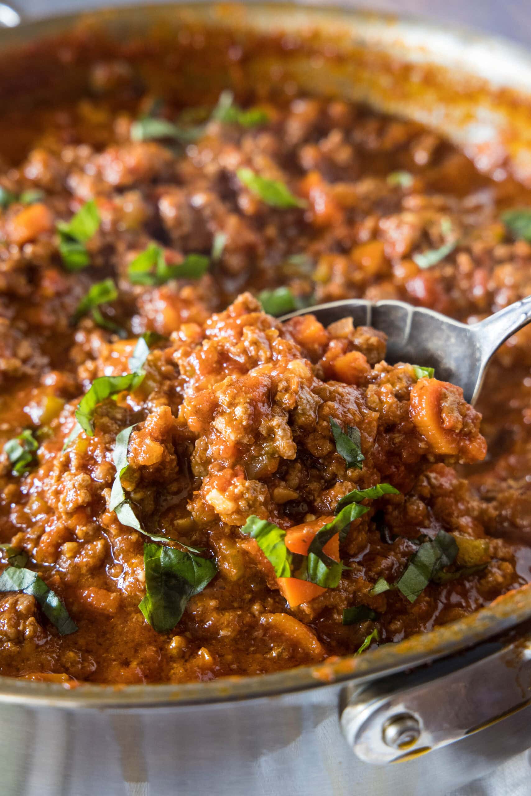 A spoon lifting beef ragu from a large deep skillet.