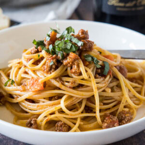 Beef ragu served with spaghetti in a white bowl.