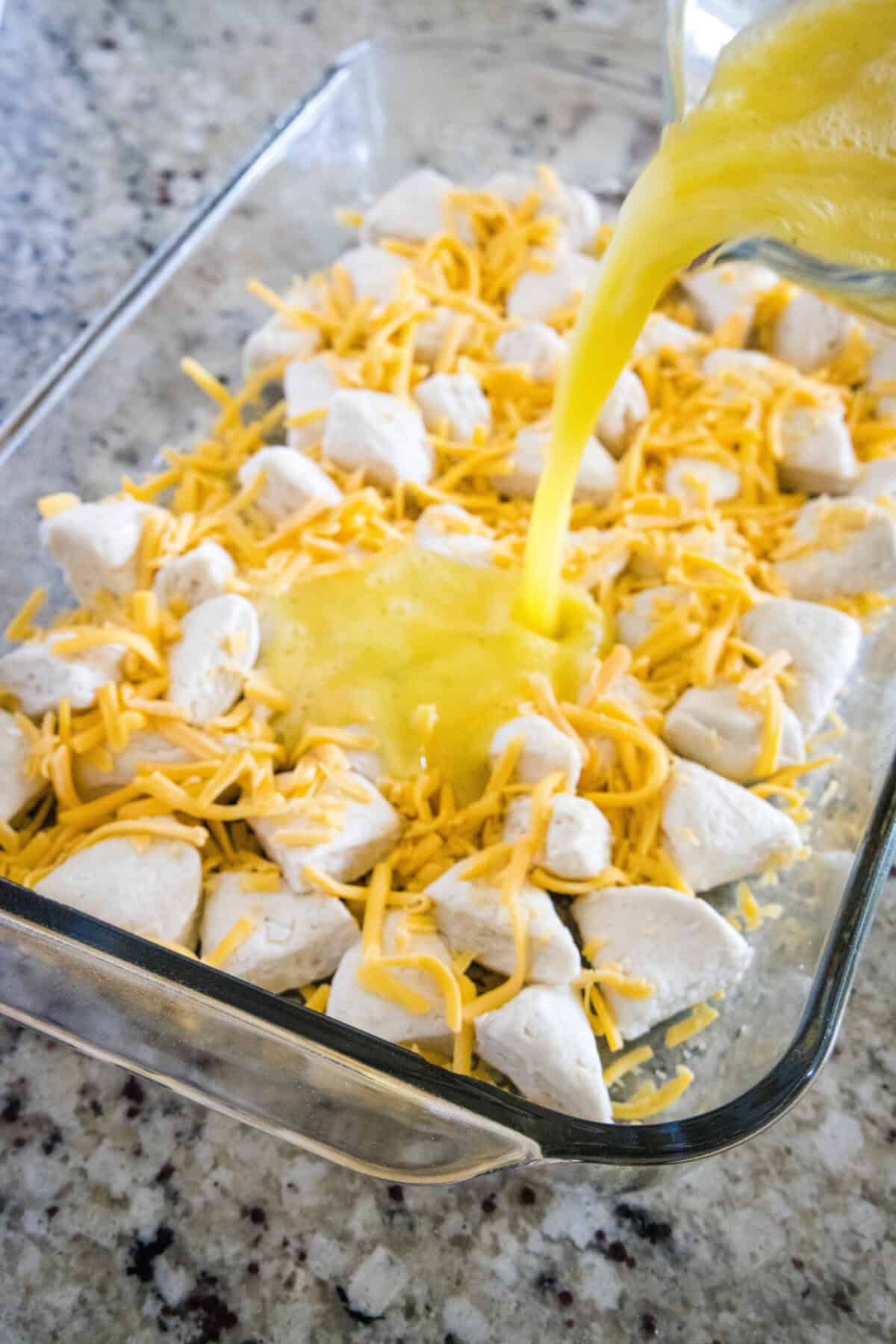 pouring egg mixture over biscuits and cheese