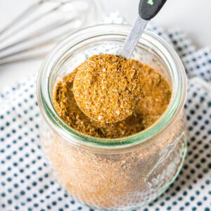 close up teaspoon of seasoning above a spice jar