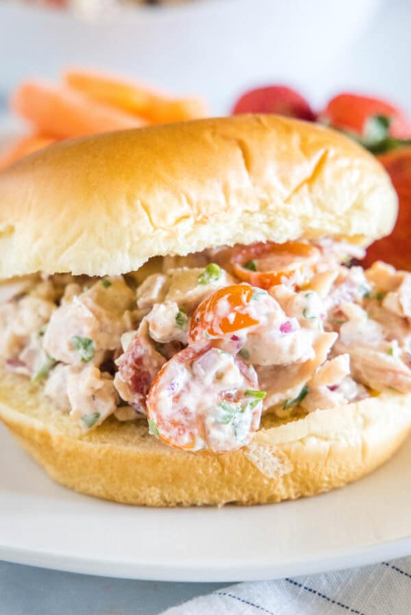 A BLT chicken salad sandwich on a fluffy bun on a white plate.