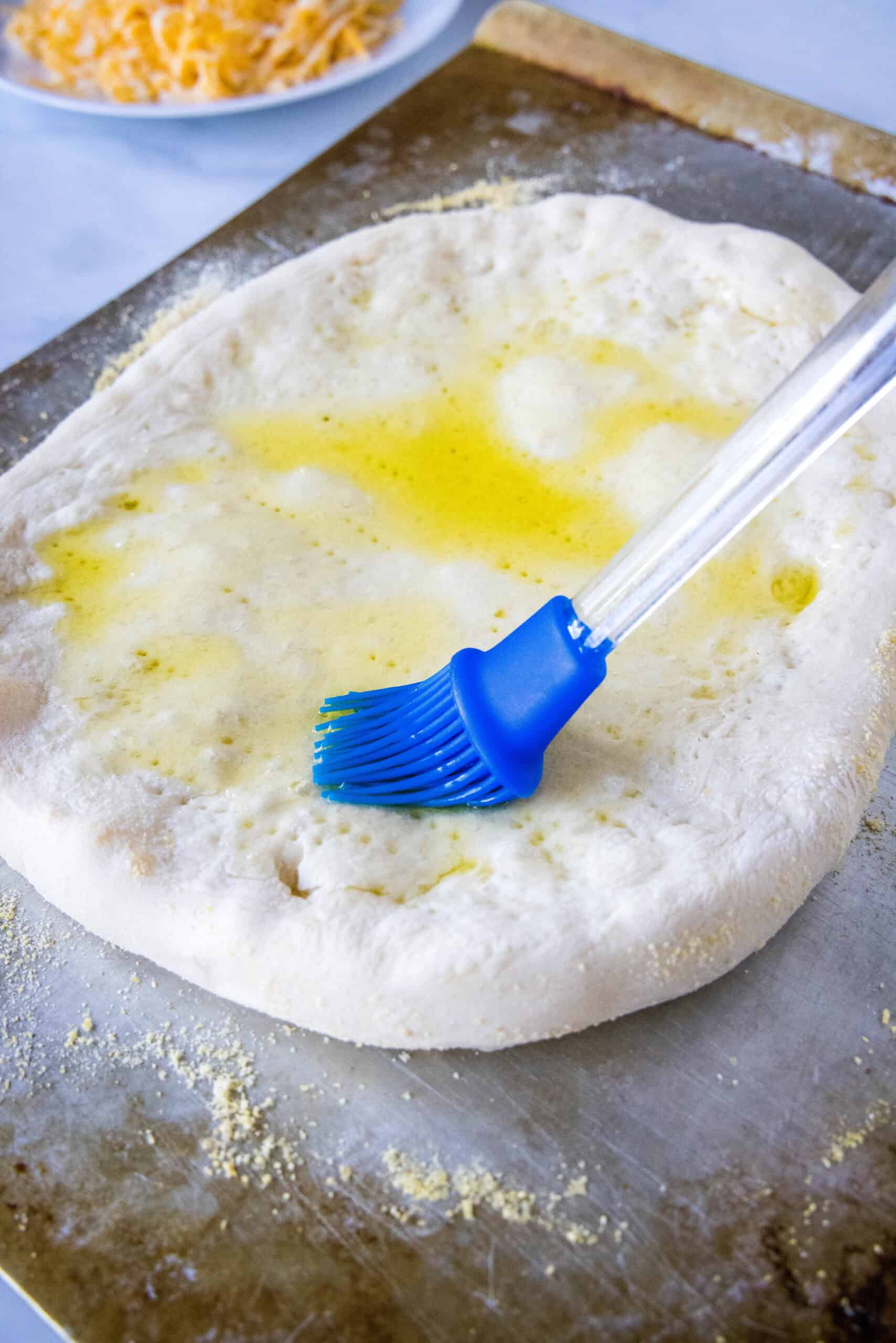 A rubber basting brush coating the top of a par-baked crust with olive oil.
