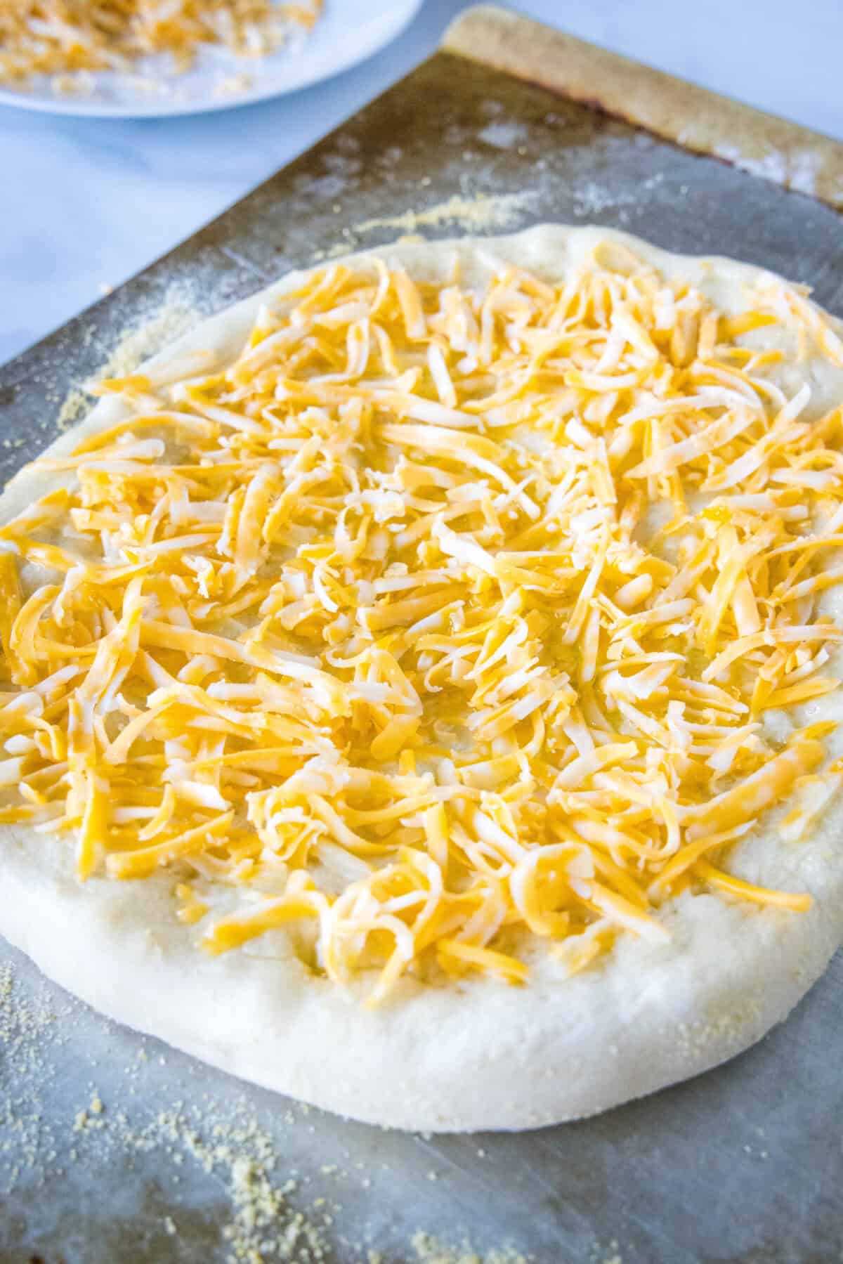 A par-baking pizza crust topped with shredded cheese on a baking sheet.