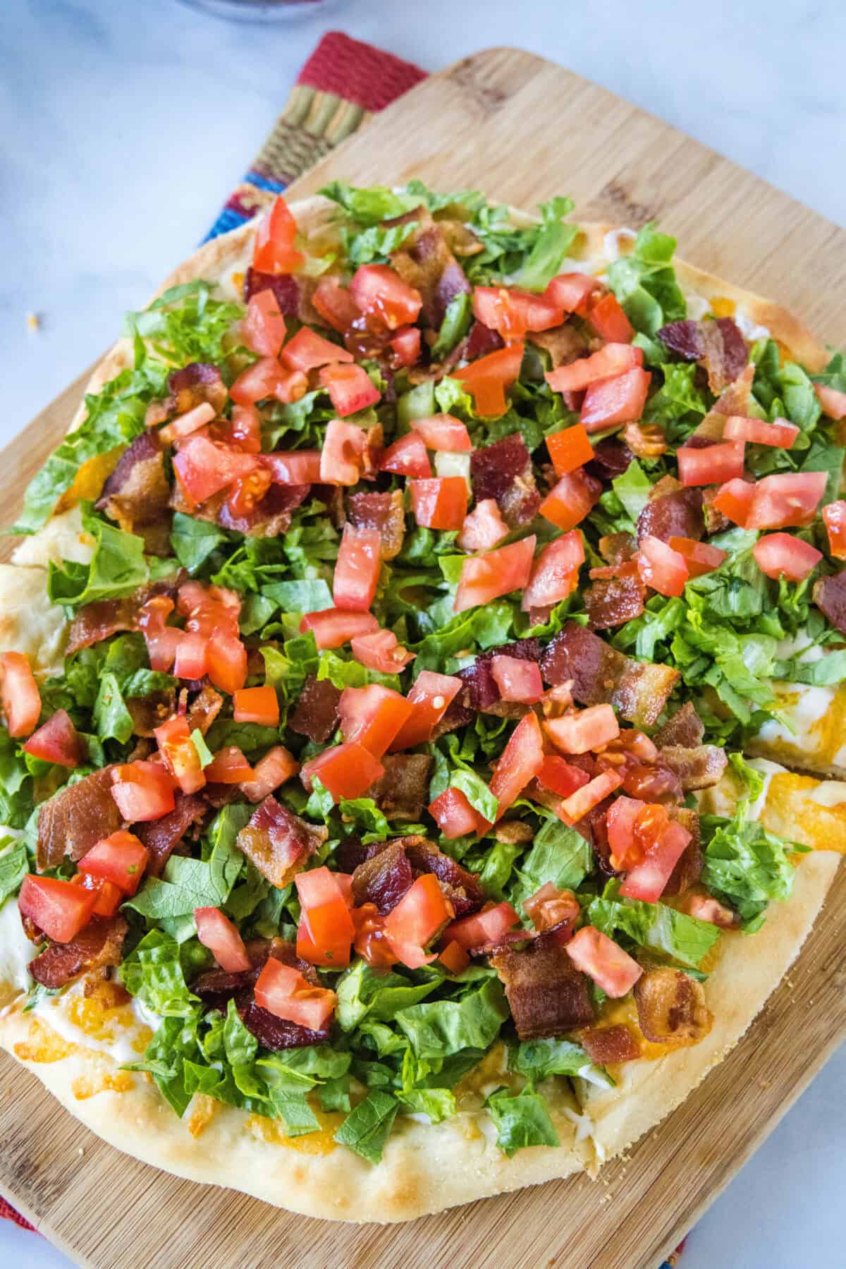 Overhead view of a BLT pizza on a wooden cutting board.