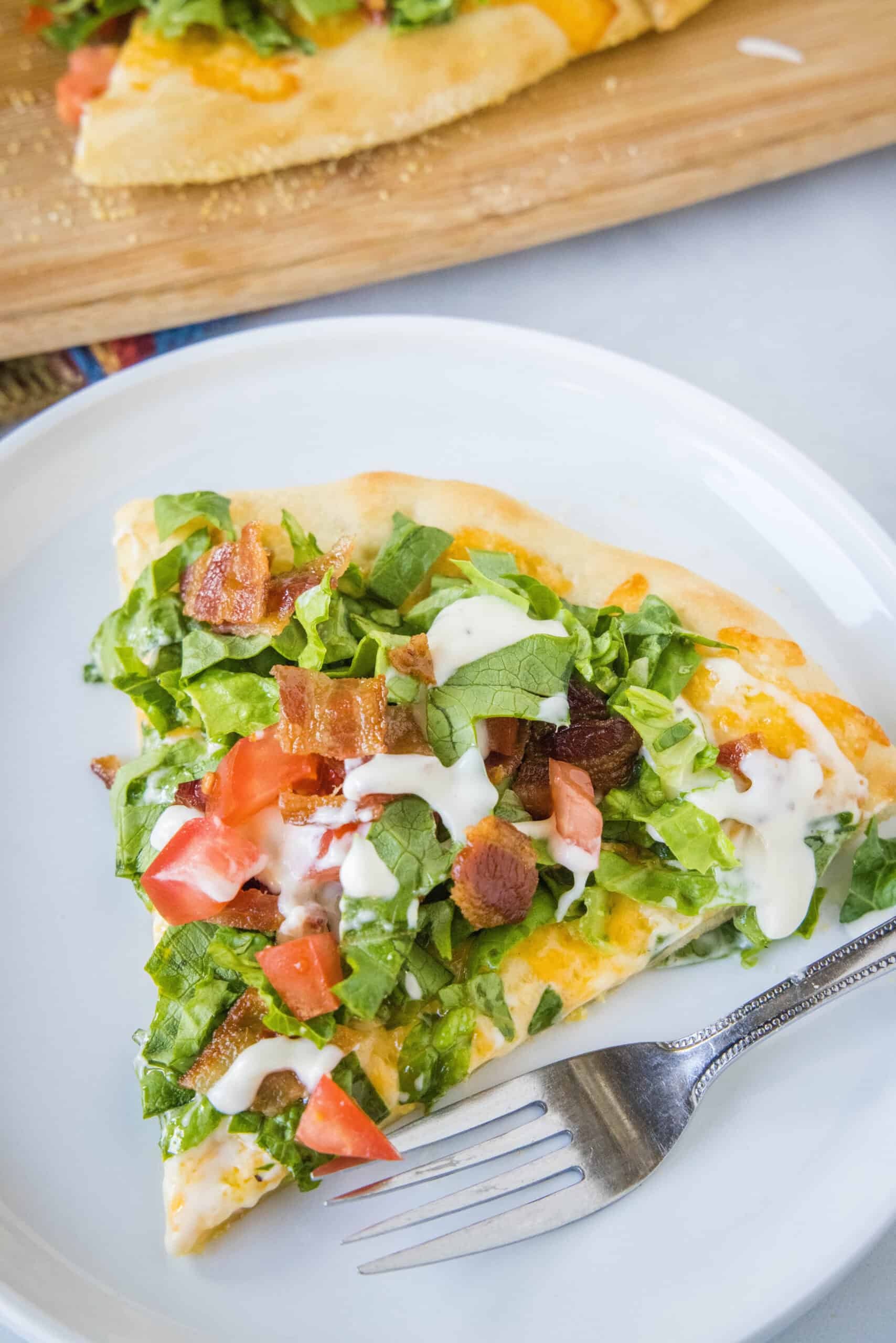 A slice of BLT pizza on a white plate next to a fork.