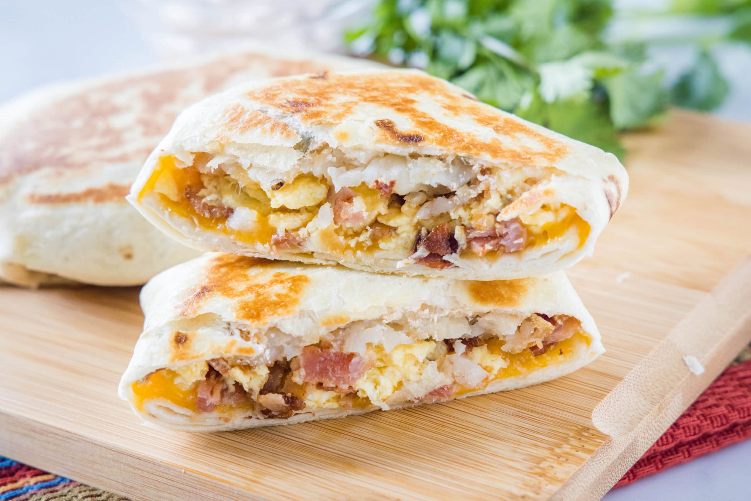 Two halves of a breakfast crunchwrap stacked on top of one another on wooden cutting board.