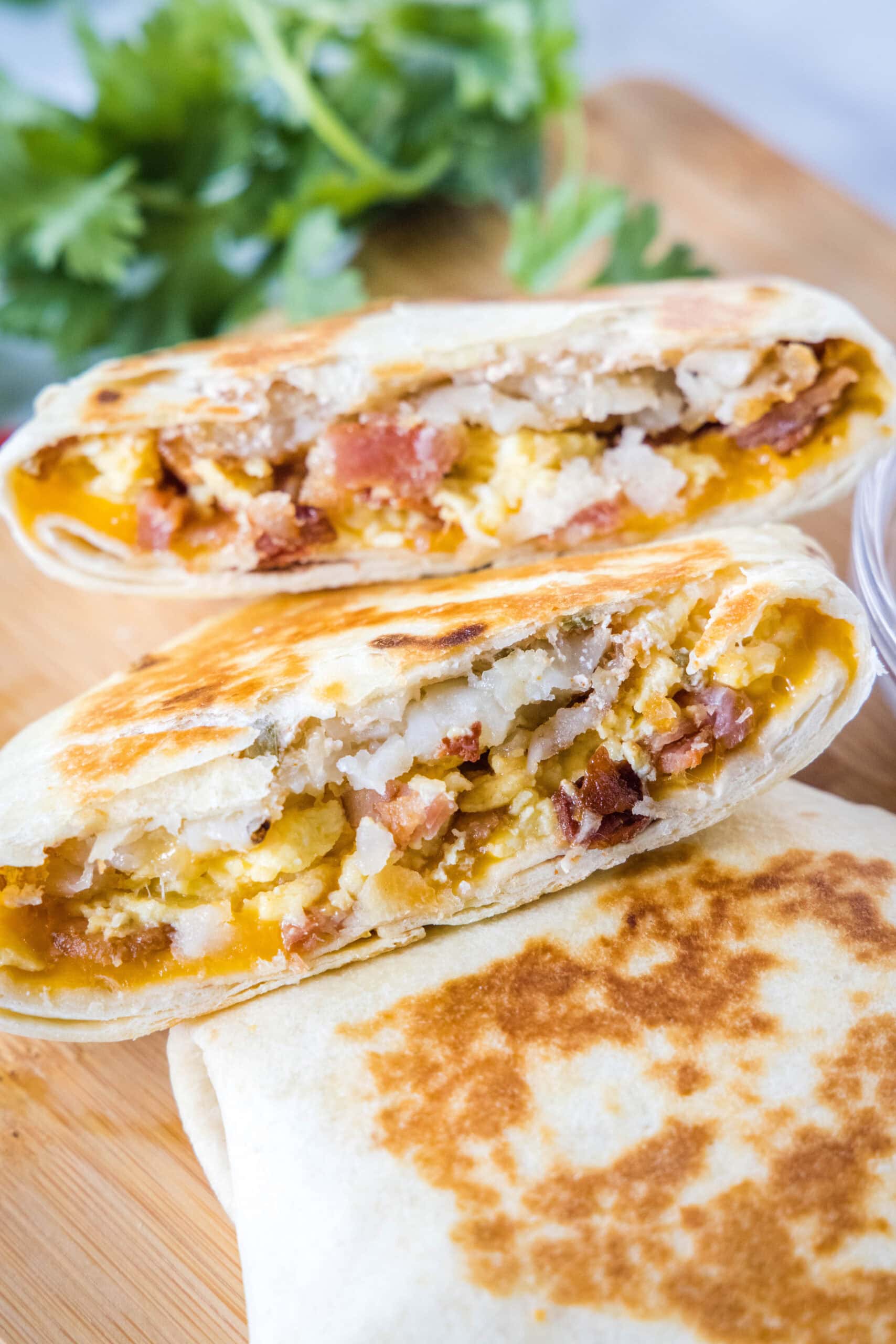 Two halves of a breakfast crunchwrap stacked on a second crunchwrap on wooden cutting board.