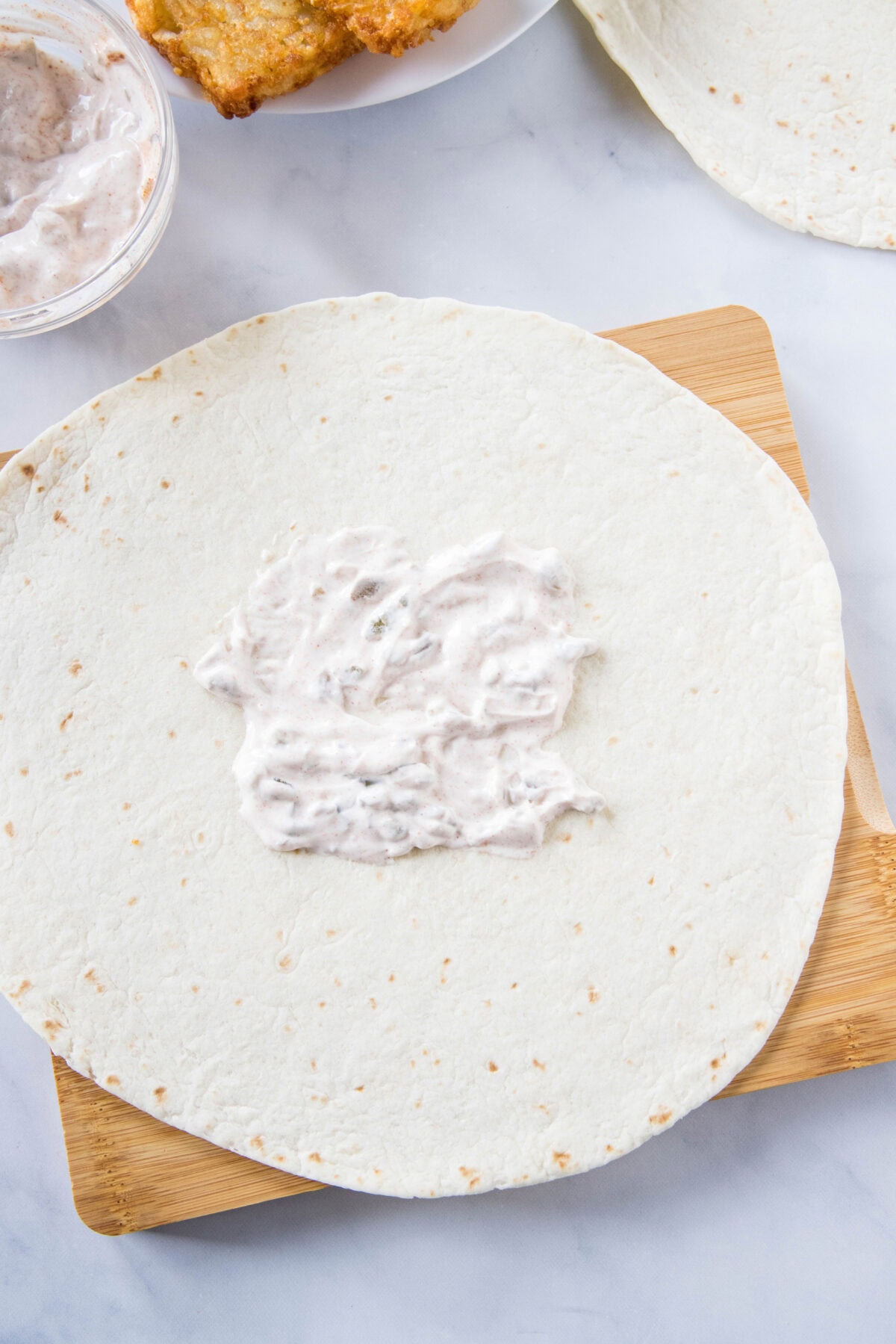 Creamy jalapeño sauce spread in the center of a large flour tortilla.